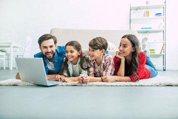 Beautiful modern young family lying on the floor at home and doing something in laptop