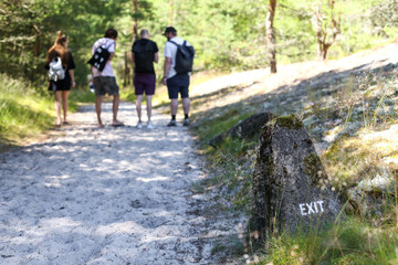 Exit sign on a stone. Four people standing in the background on a path to the beach. In Nida, Lithuania, in curonian spit.