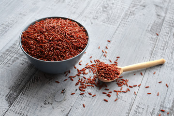Bowl and full spoon with uncooked red rice on wooden background