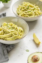 Pasta with avocado and Greek basil sauce in a ceramic bowl on a white table. Dinner for two, copy space.