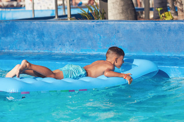 Naklejka premium Caucasian boy having fun in swimming pool at resort. He is using inflatable mattress.