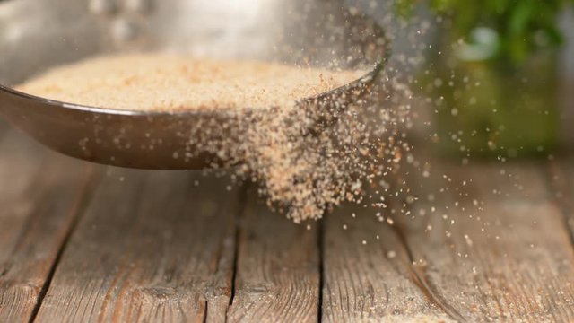 SLOW MOTION, MACRO, DOF: Heap of stale bread crumbs getting toasted in a metal pan. Unrecognizable chef roasting grated bread and crackers above a wooden table. Breadcrumbs falling onto the counter.