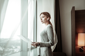 Blonde-haired woman wearing earphones standing near window