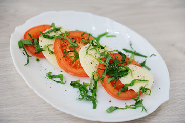 Caprese salad on a white plate. Large slices of tomatoes, mozzarella cheese and basil greens