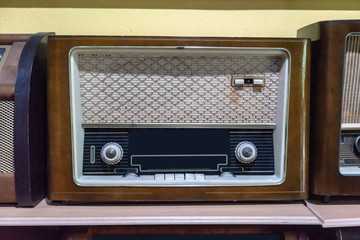 Retro broadcast radio receiver on wooden shelf against yellow background.