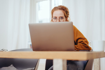 Girl peeping out from behind laptop screen