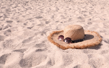 Fototapeta na wymiar Straw hat with sunglasses on sandy beach. Space for text