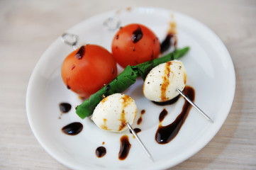 Creative serving of caprese salad. Whole tomato, mozzarella cheese ball, green basil leaf on skewers. Balsamic sauce