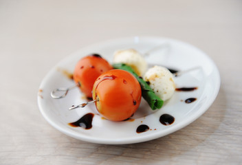 Creative serving of caprese salad. Whole tomato, mozzarella cheese ball, green basil leaf on skewers. Balsamic sauce