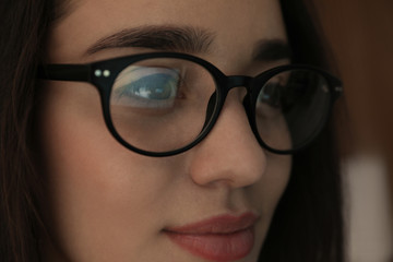 Beautiful young woman wearing glasses on blurred background, closeup. Ophthalmologist service