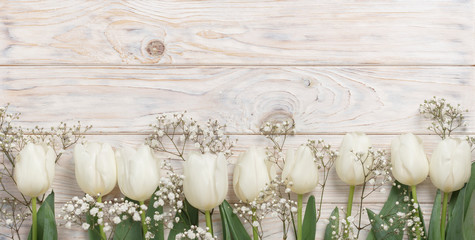 White tulips on a light wooden background. View from above.