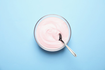 Glass bowl with creamy yogurt and spoon on color background, top view