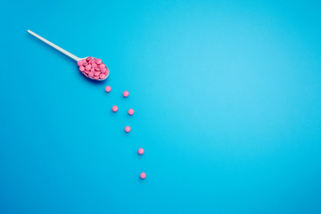 Pills tablet spilling out spoon on blue background, medicine and drug concept