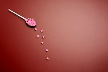 Different pharmaceutical medicine pills, tablets in spoon on red background. Pharmacy, treatment and drugs prescription theme, medicine concept