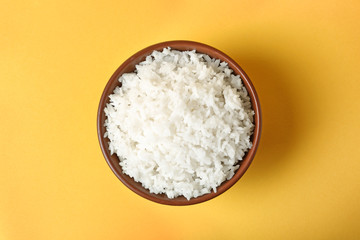 Bowl of boiled rice on color background, top view