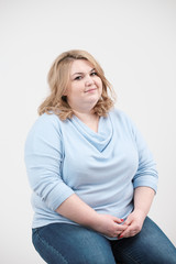Young obese woman in casual blue clothes on a white background in the studio. Bodypositive.