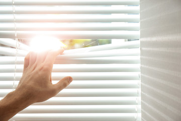 Young man opening window blinds, closeup. Space for text