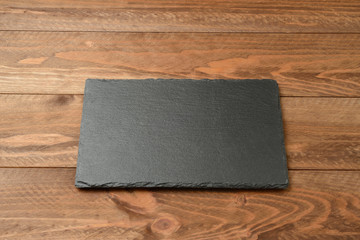 Plato de pizarra vacío en la mesa de madera marrón