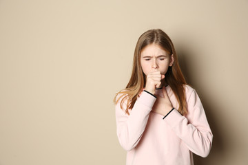 Teenage girl suffering from cough on color background. Space for text