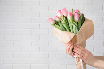 Fototapeta na wymiar Girl holding bouquet of beautiful spring tulips near brick wall, closeup with space for text. International Women's Day
