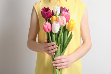 Girl holding bouquet of beautiful spring tulips on light background, closeup. International Women's Day