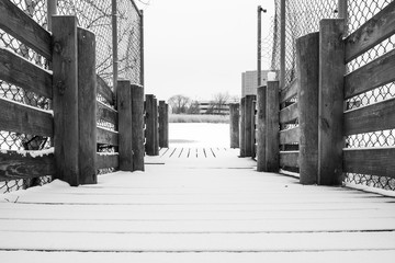 Minimal snow covered outdoor wooden pier. Winter season frozen lake river background. Park pier walkway with snow. Snow covered jetty.