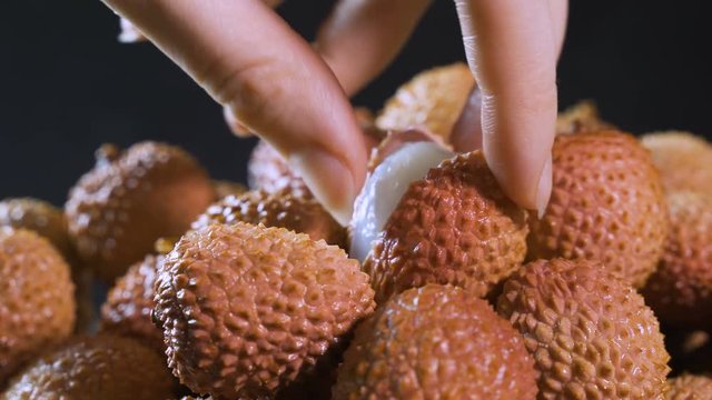 The girl's hand takes ripe juicy lychee fruits on a black background