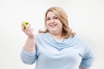 Young curvy fat woman in casual blue clothes on a white background holding a green apple in her hand. Diet and proper nutrition.