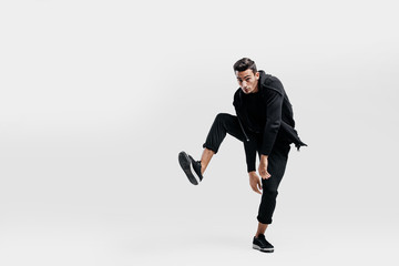 Young man dressed in a stylish black clothes lifts one leg up while dancing street dance
