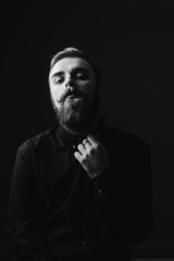 Black and white portrait of a stylish man with a beard and stylish hairdo dressed in the black shirt on the black background