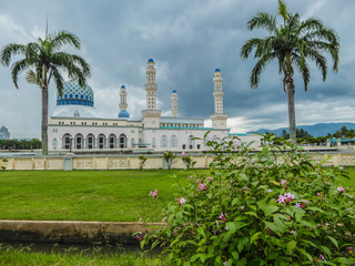 Obraz premium Masjid Bandaraya in Kota Kinabalu, Sabah, Malaysia. Lush green lawn in front of the mosque. Two palm trees on the sides of the temple. A flower bush in front. Huge overcast, storm is coming.