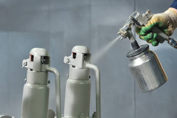 A worker at a factory in a special room paints parts of the valves from the spray gun. Paint valves...