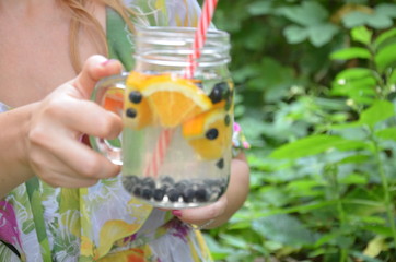 a female hand holds Glasses of detox water with sliced fruit, berries an orange and blueberries water of green foliage. cocktail or lemonade. The concept of health, diet, weight loss, clean of toxins