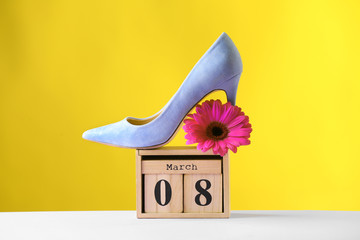 Stylish lady's shoe, flower and wooden block calendar on table against color background. International Women's Day