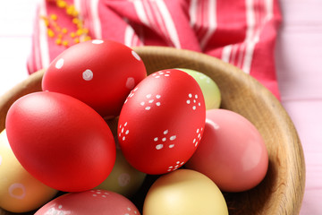 Bowl with colorful painted Easter eggs on table, closeup