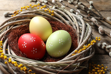 Colorful painted Easter eggs in wicker nest on table, closeup
