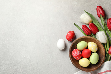 Flat lay composition of painted Easter eggs and spring flowers on light background, space for text