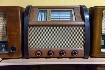 Retro broadcast radio receiver on wooden shelf against yellow background.