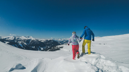 Mölltaler Gletscher,Austria. Couple playing in the fresh snow. Holding hands and getting ready to jump off the snowdrift. Skier and snowboarder. Bright skiing outfits. Endless chains of mountains.