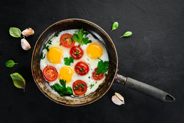 Eggs with tomatoes and greens in a frying pan.
