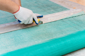 A worker is cutting  a fiberglass mesh.