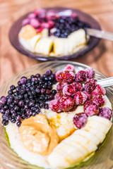 Macro closeup of two oatmeal oat grain porridge bowl with sliced bananas, peanut butter, frozen berries raspberries blueberries and topping of maple syrup