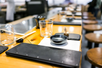 Fototapeta na wymiar Japanese restaurant in traditional style, interior asian sushi wooden bar counter, menu, bowl, glass napkin generic typical setting empty nobody closeup