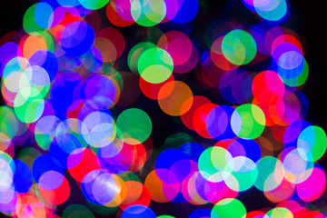 Christmas bokeh abstract background with red, blue and green, orange circles illuminated decoration lights on tree at blurry blurred night evening dark black