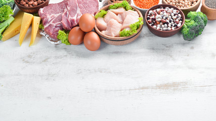 Balanced diet food background. Meat, chicken fillet, broccoli, beans, cheese, eggs, wheat. On a white wooden background.