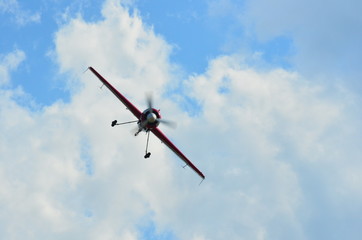 Fototapeta na wymiar Front view of a stunt monoplane flying on cloudy blue sky leaving white smoke trail