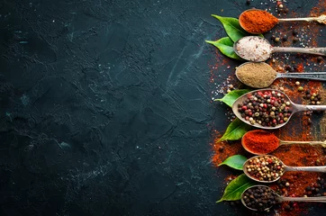 Fotobehang Pepper in a spoon. Colored pepper, sea salt, ground pepper, chili pepper. Top view. On a black background. © Yaruniv-Studio