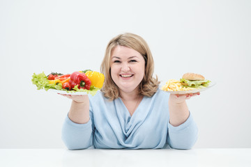 Young lush fat woman in casual blue clothes on a white background holding a vegetable salad and a...