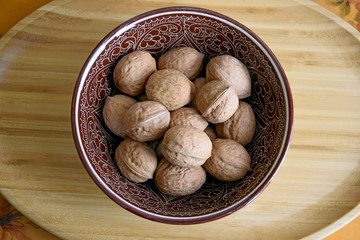 walnuts in a ceramic bowl on a wooden tray close-up, top view