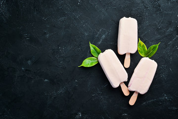Ice-cream on a stick with white chocolate. On a black background. Top view. Free copy space.